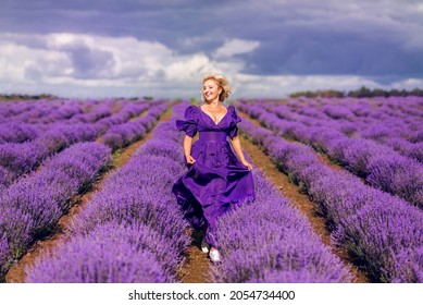 An elderly woman walks in a field of lavender. Beautiful senior in a purple dress runs in lavender.