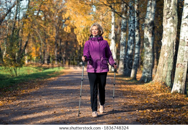 an elderly woman walks through the Park on\
Scandinavian sticks