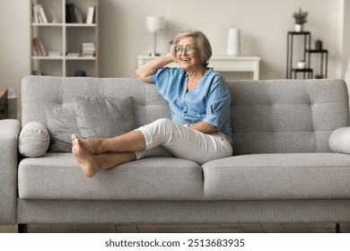 Elderly woman wear casual clothes sitting on sofa in modern living room, smile, enjoy quiet, serene and joyful moments alone at own apartment spend time in cozy home environment. Relaxation, comfort - Powered by Shutterstock