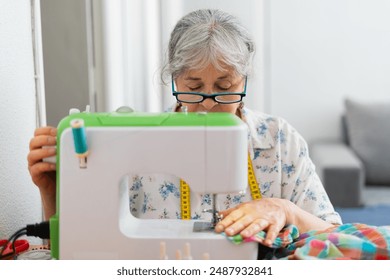 Elderly woman in a wheelchair focused on sewing fabric on a sewing machine with a measuring tape around her neck. Concept of creative sewing. - Powered by Shutterstock