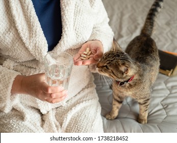 Elderly Woman In  White Terry Cloth Robe Sitting On The Bed And Washes Down The Pills With A Glass Of Water