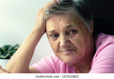 An Elderly Woman At The Window. An Old Lonely Woman Sitting By The Window In Her House. Sad Lonely Old Age.