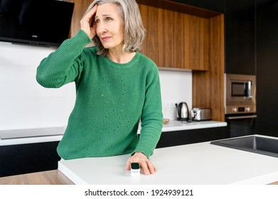 Elderly Woman With Wrinkles On The Face, Narrow Lips, With A Headache, Sensitive To Weather, Checking Blood Pressure And Pulse, Leaning On The Countertop In The Kitchen, Has An Elegant Grey Hair