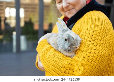 Elderly woman in a yellow sweater with a rabbit in her arms  - Powered by Shutterstock