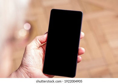 Elderly womans hand holding mobile cell phone. Over shoulder. Old woman looking at cell phone. Close-up. Blanck mobile phone screen. Display media. 