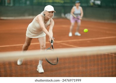 Elderly women in doubles playing tennis on tennis court - Powered by Shutterstock