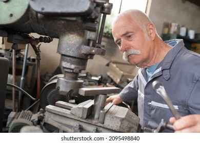 elderly worker watches processing of detail on milling machine - Powered by Shutterstock