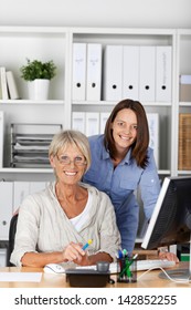 An Elderly And Young Female Smilingly Posing Inside The Office.