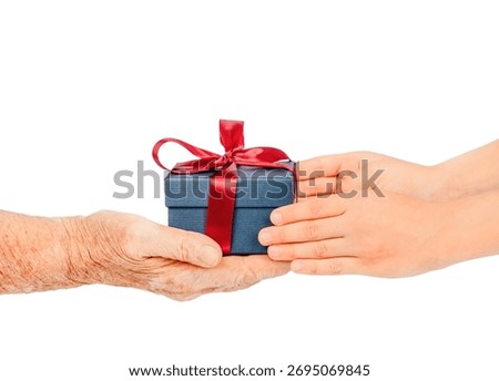Elderly and young hands exchanging a small blue gift box with a red ribbon, isolated on white. Concept of care, giving, gratitude connection between generations during holidays. special occasions.