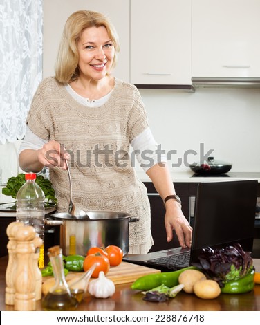 Eldery woman using notebook while cooking vegetables at home kitchen