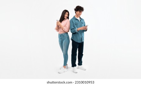 E-Learning Apps. Young Couple Using Mobile Phones Texting And Communicating In Social Media, Standing On White Studio Background. Smiling Girlfriend Peeking At Boyfriend's Smartphone. Panorama