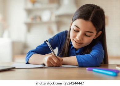 E-Learning. Arabic School Girl Writing Notes While Studying With Laptop Sitting At Table At Home. Cute Preteen Kid Doing Homework Online And Noting Information From Internet Lecture Near Computer - Powered by Shutterstock