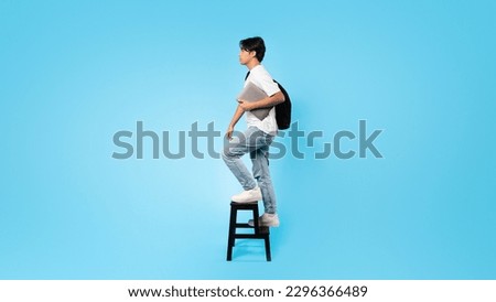 E-Learning Concept. Japanese Teen Guy Holding Laptop Computer Walking Upstairs On Ladder Posing On Blue Studio Background. Online Education Concept. Full Length, Panorama