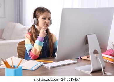 E-learning. Cute girl using computer and headphones during online lesson at table indoors