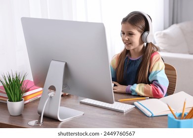 E-learning. Cute girl using computer and headphones during online lesson at table indoors - Powered by Shutterstock