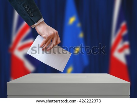 Election or referendum in Great Britain. Voter holds envelope in hand above vote ballot. British and European Union flags in background.