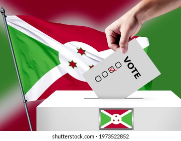 Elections In The Burundi. The Hand That Puts The Game In The Ballot Box. Burundi Flags In The Background. Country Flag Election.