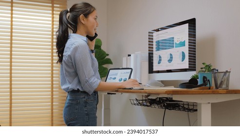 Electric adjustable standing desk in small office workspace for PC desktop computer worker. Asia people young woman relax remote work at home proper height up workstation physical workforce challenge. - Powered by Shutterstock