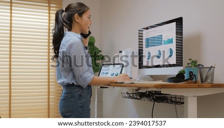 Electric adjustable standing desk in small office workspace for PC desktop computer worker. Asia people young woman relax remote work at home proper height up workstation physical workforce challenge.