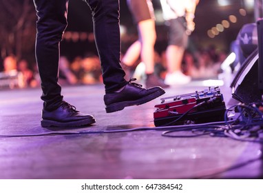 Electric bass guitar player on a stage with set of distortion effect pedals under his foot. - Powered by Shutterstock