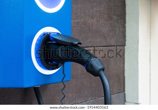 Electric car charger with blue electric car\
charging station on city street. Close up of power supply plugged\
into a power socket\
