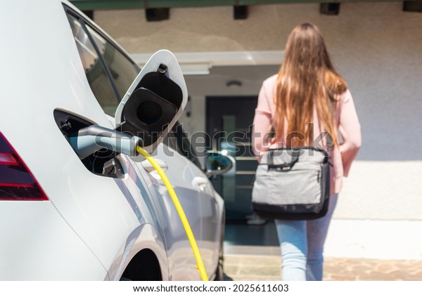 Electric car charger plugged in, with a female\
silhouette in the\
background