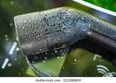 A Electric Car Charger With Water Droplets. Reflection Of Urban Greenery. Car Charging Station. Online Shopping. Rain Protection 