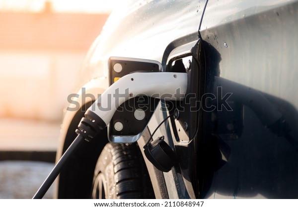 A electric car charging with a charging cable\
plugged in on a sunny day. 