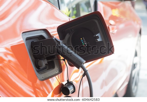 Electric car charging on parking lot with\
electric car charging station on city street. Electric cars in the\
row ready for charge. Close up of power supply plugged into an\
electric car being\
charged.