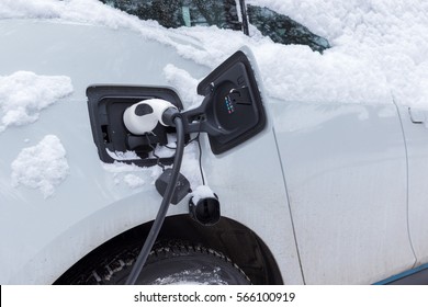 Electric Car Charging. Car And Socket Covered By Snow In Winter Time