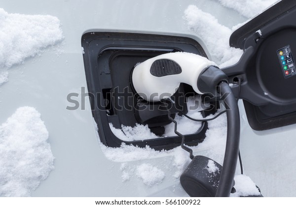 Electric car charging. Car and socket covered by\
snow in winter time