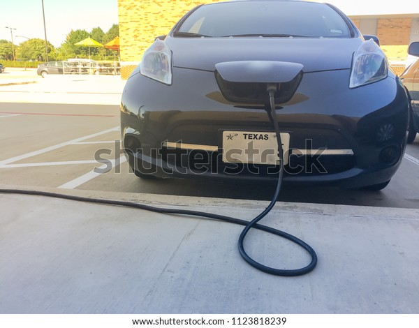 Electric car at\
charging station with charger plugged into the hood. Rechargeable\
batteries vehicle refuel at parking lots. Concept of future\
automobile and\
transportation