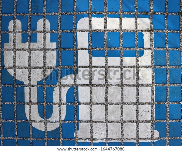 Electric\
car charging station sign painted on tiles of parking place. White\
electric  pump silhouette on blue\
background.