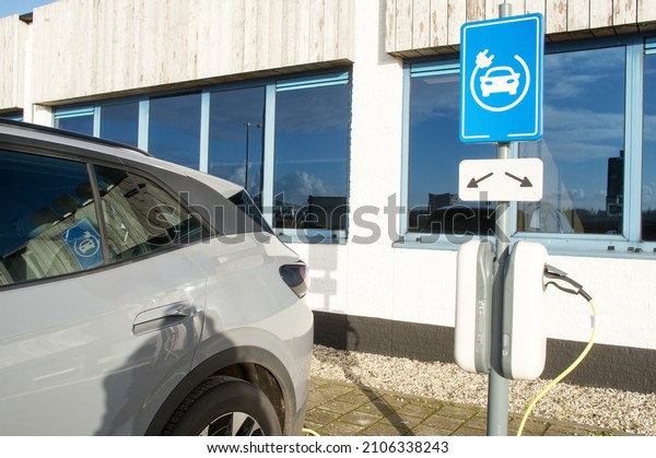 Electric car connected to charge\
station for charging the battery with a blue charge station\
sign