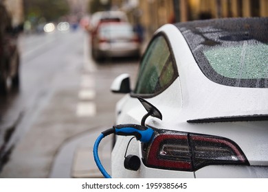 Electric Car Is Connected To The Charging Station  Electric Vehicle Standing In The Rain In Munich City