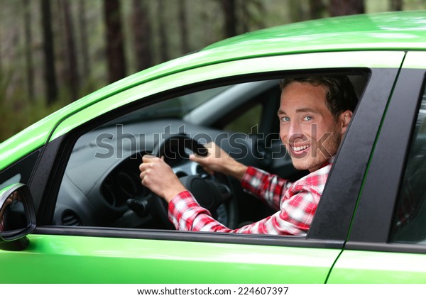 Electric car driver - green energy biofuel\
concept. Male behind wheel. Man driving new ecofriendly vehicle in\
nature forest. Young male owner proud confident looking at camera,\
Taxi driver concept.