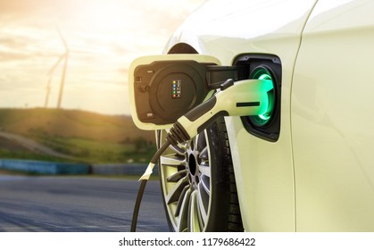 Electric car or EV car charging in station on blurred of sunset with wind turbines in front of car on background.  Eco-friendly alternative energy concept - Shutterstock ID 1179686422