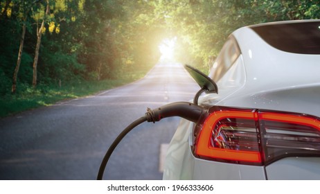 Electric Car Or EV Car Charging In Station On Asphalt Road In Morning Time Background. Eco-friendly Alternative Energy Concept