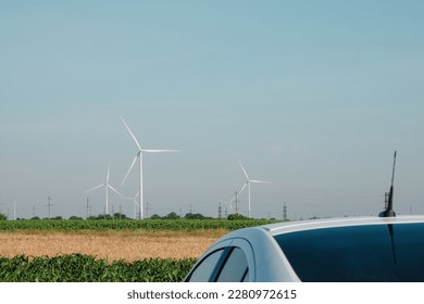Electric car roof standing in countryside among windmill windfarms. Automobile stands against distant wind turbines on field - Shutterstock ID 2280972615
