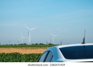 Electric car roof standing in countryside among operating windmills on windfarm. Automobile stands against distant wind turbines on field - Shutterstock ID 2282471929