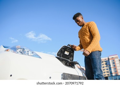 Electric Cars, EV Concept, Eco Friendly Fuel. Portrait Of Young Smiling Black Man, Recharging His Modern Luxury Electric Car