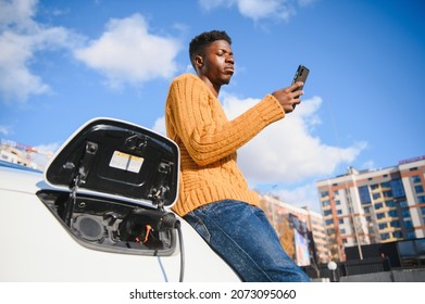 Electric Cars, EV Concept, Eco Friendly Fuel. Portrait Of Young Smiling Black Man, Recharging His Modern Luxury Electric Car