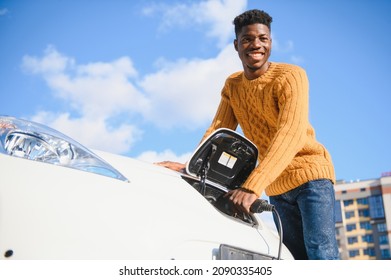 Electric Cars, EV Concept, Eco Friendly Fuel. Portrait Of Young Smiling Black Man, Recharging His Modern Luxury Electric Car