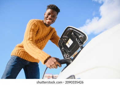 Electric Cars, EV Concept, Eco Friendly Fuel. Portrait Of Young Smiling Black Man, Recharging His Modern Luxury Electric Car