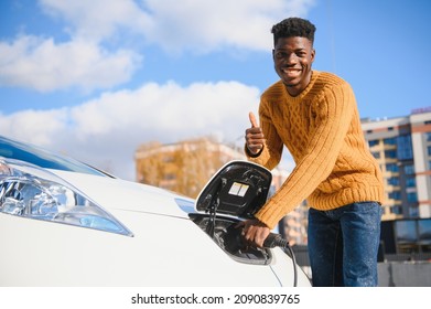 Electric Cars, EV Concept, Eco Friendly Fuel. Portrait Of Young Smiling Black Man, Recharging His Modern Luxury Electric Car