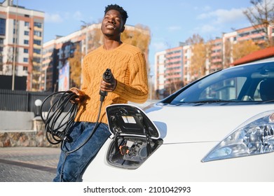 Electric Cars, EV Concept, Eco Friendly Fuel. Portrait Of Young Smiling Black Man, Recharging His Modern Luxury Electric Car