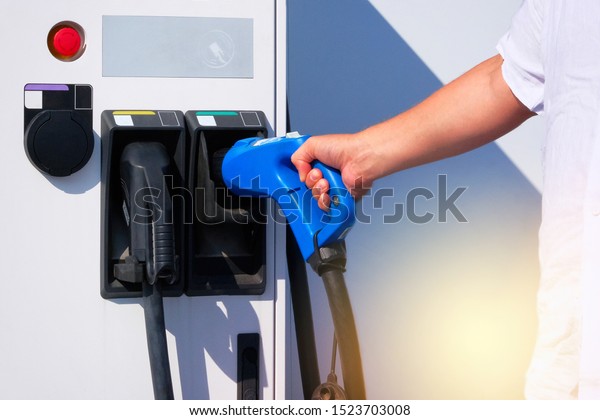 Electric charging station. Hand of\
driver is holding charger for electric cars on city parking. Eco\
friendly transport concept. Modern alternative\
energy.