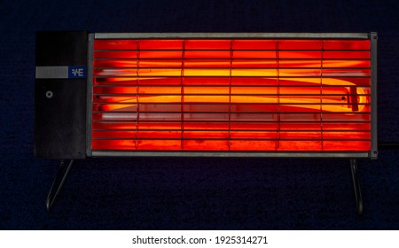 Electric Coil Heater Glowing Orange In The Dark Room.
