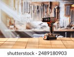 Electric cordless drill screwdriver tool on wooden work table in craft workshop. Blurred wall with tools in the background. Empty advertising copy space for product mountage.