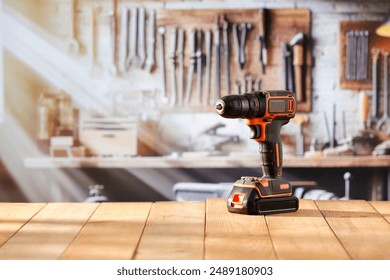 Electric cordless drill screwdriver tool on wooden work table in craft workshop. Blurred wall with tools in the background. Empty advertising copy space for product mountage. - Powered by Shutterstock